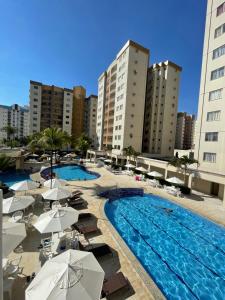 une piscine avec des parasols et des chaises ainsi que certains bâtiments dans l'établissement Flat Prive das Thermas II - R3 Caldas, à Caldas Novas