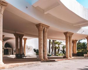 Kanta Resort and Spa في سوسة: صف من الاعمدة في مبنى فيه نخيل