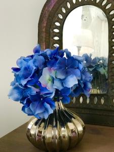 un vase rempli de fleurs bleues devant un miroir dans l'établissement Fleur de Lis, à Belas