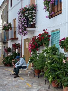 un hombre sentado en una silla frente a un edificio con flores en Calle Horno, en Castril