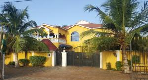 una casa gialla con un cancello nero e palme di Coconut Pointe Villa & Beach Resort a Prampram