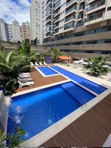uma piscina azul com cadeiras e um edifício em Flat Capitania Varam no Guarujá