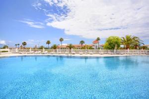 a large swimming pool with a white fence and palm trees at El Veril 84 Bahia del Duque in Adeje