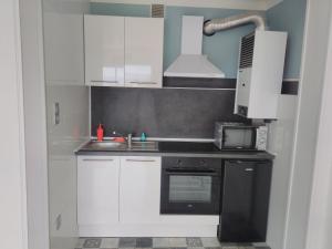 kuchnia z białymi szafkami, zlewem i kuchenką mikrofalową w obiekcie Residence d'Anjou - Grand studio avec balcon et parking privatif w Perpignanie