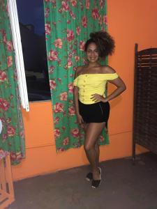 Perto Do Aeroporto De Salvador - Dona Pitanga Hostel في لورو دي فريتاس: امرأة في قمة صفراء تقف في غرفة