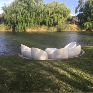 un grupo de sillas blancas sentadas en la hierba junto al agua en Cabañas Rio Soñado en Valle Grande