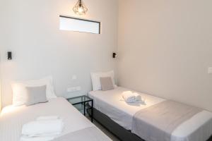 two twin beds in a room with white walls at Porto Bello Tinos in Agios Ioannis