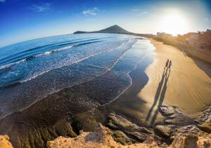 two people standing on a beach near the ocean at MEDANO4YOU Cabezo at Marineda in El Médano