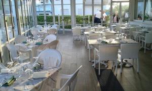 un restaurante con mesas blancas, sillas blancas y ventanas en Oasi Verde, en Lido di Jesolo
