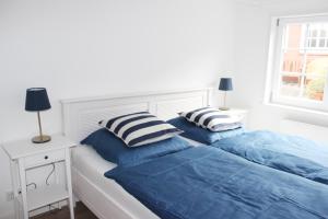a white bedroom with a bed with blue sheets and a window at Haus Frisia Ferienwohnung Frisia 3 in Norddorf