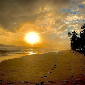 a sunset on a beach with footprints in the sand at Mirage Beach House at Morava Court in Hikkaduwa