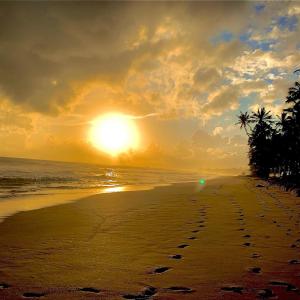 a sunset on a beach with footprints in the sand at Virage Beach House @ Morava Court in Hikkaduwa