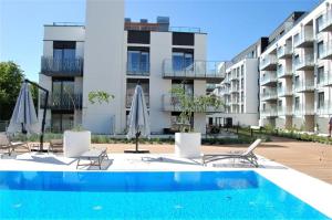 a pool with chairs and umbrellas in front of a building at Bodnar Apartamenty Nadmorskie Tarasy Port in Kołobrzeg