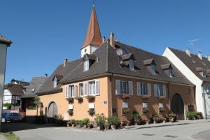 a yellow building with a spire on a street at Au Petit Paradis in Ammerschwihr