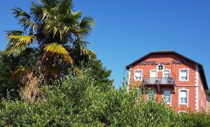 a red building with a balcony and a palm tree at Hotel de La Paix in Oloron-Sainte-Marie