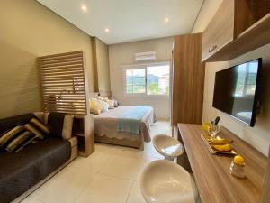 a bedroom with a bed and a couch and a television at Happy Flat Itaipava - Granja Brasil in Itaipava