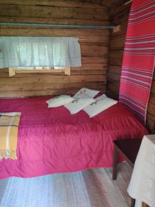 a bed in a wooden cabin with pink sheets at Haaran torppa in Mikkeli