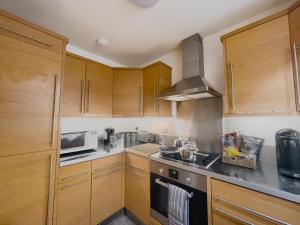 a kitchen with wooden cabinets and a stove top oven at Spacious Contractor Flat for Large groups - Private Parking by Tailored Apartments in Cheshunt
