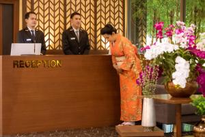 是拉差Hotel Kuretakeso Thailand Sriracha - SHA Extra Plus的站在前台后面的一位身着橙色衣服的女人