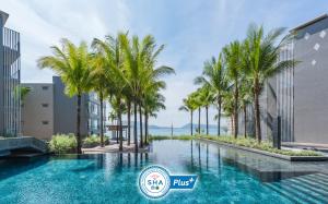 a pool with palm trees in front of buildings at Oceanfront Beach Resort - SHA Extra Plus in Patong Beach