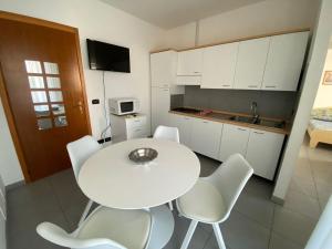 cocina blanca con mesa blanca y sillas blancas en Appartamenti al Cigno, en Lignano Sabbiadoro