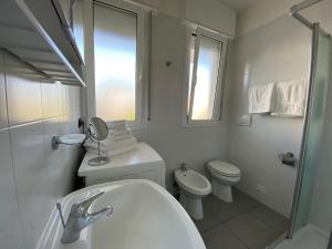 Baño blanco con aseo y lavamanos en Appartamenti al Cigno, en Lignano Sabbiadoro