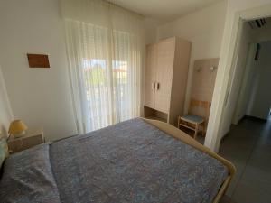 1 dormitorio con cama, ventana y silla en Appartamenti al Cigno, en Lignano Sabbiadoro