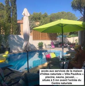 une femme assise sous un parasol à côté d'une piscine dans l'établissement Studio Naturiste PaulAna Héliopolis L39, au Cap d'Agde