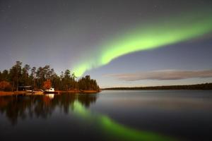 una aurora sobre un lago por la noche con las estrellas en Wilderness Hotel Nellim & Igloos en Nellimö