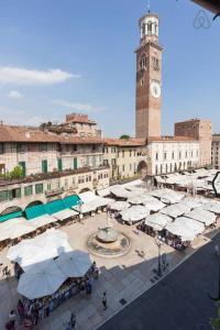 a city square with a clock tower and a building with white tents at Truly Verona - Delle Erbe suites in Verona