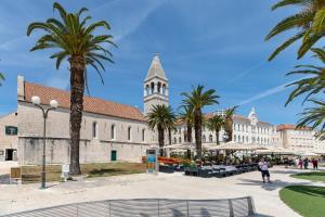 a building with a clock tower and palm trees at Apartments and Rooms Mišić in Trogir
