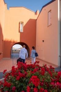 Un uomo e una donna in piedi accanto a un palazzo con fiori rossi. di Residence Marina Salivoli a Piombino