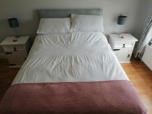un grande letto con lenzuola bianche e due comodini di An Charraig Ban on the wild Atlantic way F94WT02 a Ardara