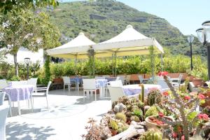 a patio with white tables and chairs and plants at Hotel Maronti in Ischia