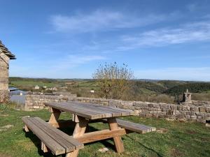 una mesa de picnic de madera sentada en el césped junto a una pared de piedra en Gîte du Dolmen de l'Hom, en Le Massegros