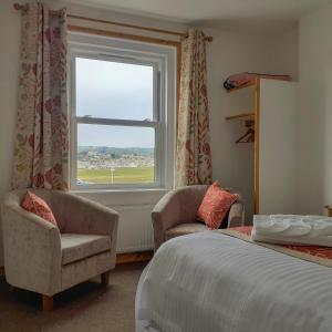 a bedroom with a bed and two chairs and a window at Links Side Guest House in Bude