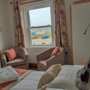 a bedroom with a bed and two chairs and a window at Links Side Guest House in Bude