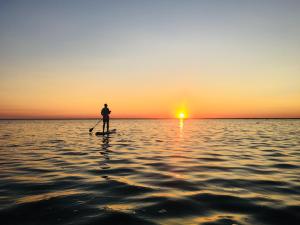 a person standing on a paddle board in the water at sunset at Abruka Glamping in Abruka