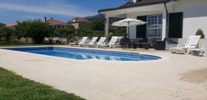 a pool with chairs and an umbrella next to a house at Quinta do Paulo in Caramulo