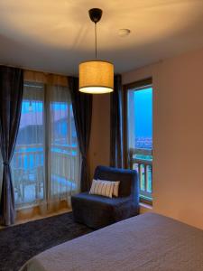 a bedroom with a bed and a chair and windows at Mirabell Apartment Bansko - Mountain View & Fireplace in Bansko