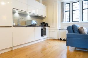 a kitchen with white cabinets and a blue couch in a room at Executive City Centre Apartment with Gated Parking and Stylish Rooms includes Privacy and Space with Luxury Feel plus Courtyard Garden in Amazing Location and Very Highly Rated in Peterborough