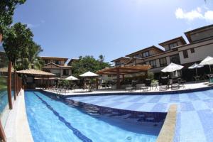 una piscina en un resort con sillas y sombrillas en Apt na Praia do Forte em Condomínio frente mar!, en Praia do Forte
