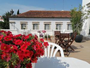 a table with red flowers in front of a house at Hostel Rossio Alcobaça in Alcobaça