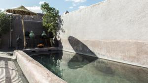 Eine Wasserlache neben einer Mauer mit einem Sonnenschirm in der Unterkunft Dar Darma in Marrakesch