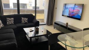 sala de estar con sofá negro y TV en Dair Ghbar Apartment, en Amán