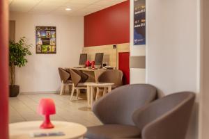 a waiting room with chairs and a table with a red wall at ACE Hôtel Rouen Parc des Expositions in Le Petit-Couronne