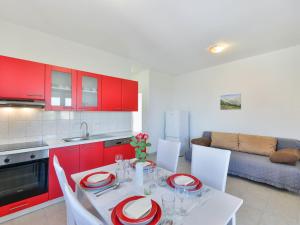 a kitchen with red cabinets and a white table with chairs at Apartment Matas-2 by Interhome in Rovanjska