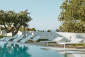 a row of white lounge chairs next to a swimming pool at Masseria Borgo Ritella in Fasano