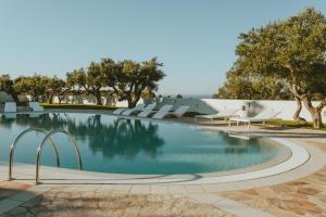 a swimming pool with chairs and trees and water at Masseria Borgo Ritella in Fasano