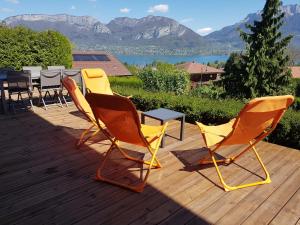 three chairs and a table on a wooden deck with mountains at Appartement Semnoz - Vue Lac in Sévrier